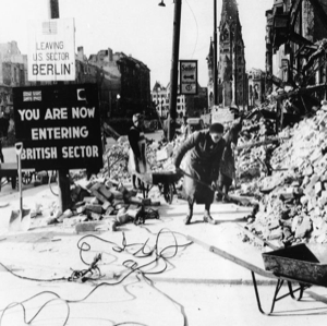 Black and white photo of woman looking at rubble near British/Berlin sign