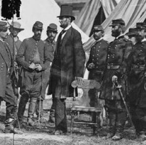 Photo of Lincoln with hand on a chair and a group of male soldiers behind him