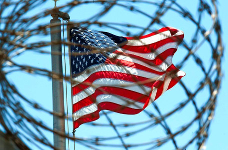 Photo of U.S. flag as seen through barbed wire at the Guantanamo Bay detention facility.