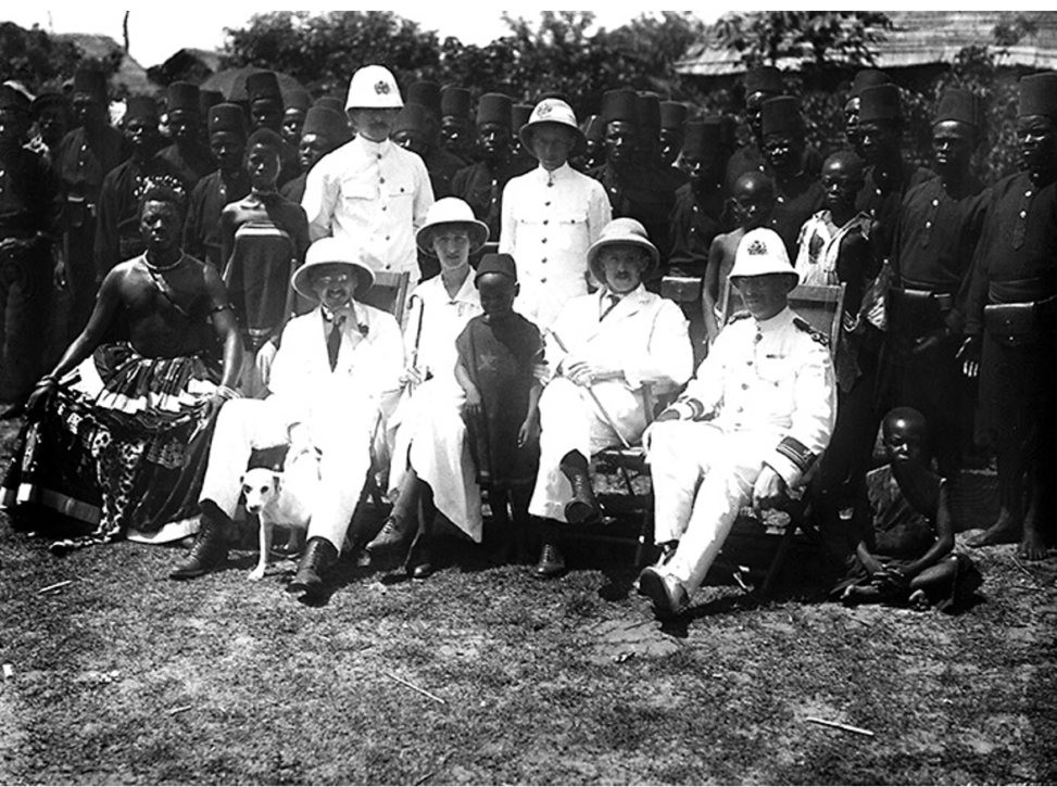 Black and white photograph with figures dressed all in white sitting in front of figures dressed all in black standing behind them.