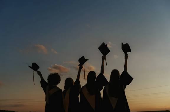 four students raising their graduation caps in to the air