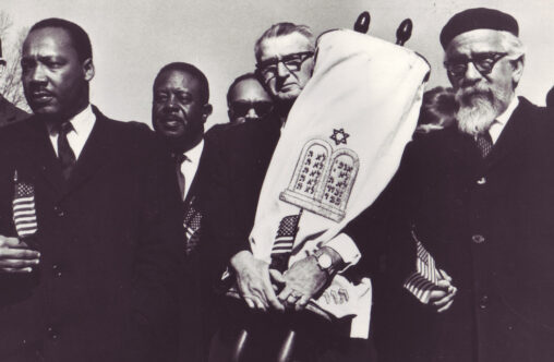 Two rabbis march with Martin Luther King, Jr. One holds a torah, the other holds a small American flag.