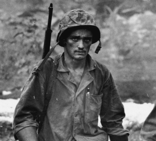 Black and white photo of soldier in military combat gear looking weary towards the camera.